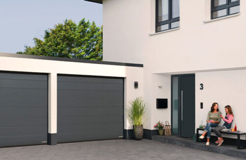 Blick auf Doppelgarage neben Hauseingang. Frau und Kind auf Bank neben Tür.